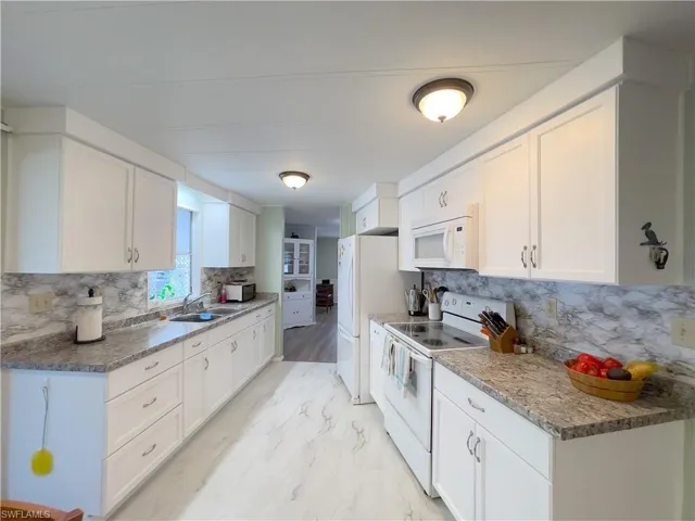 Kitchen featuring white appliances, white cabinets, tasteful backsplash, and sink