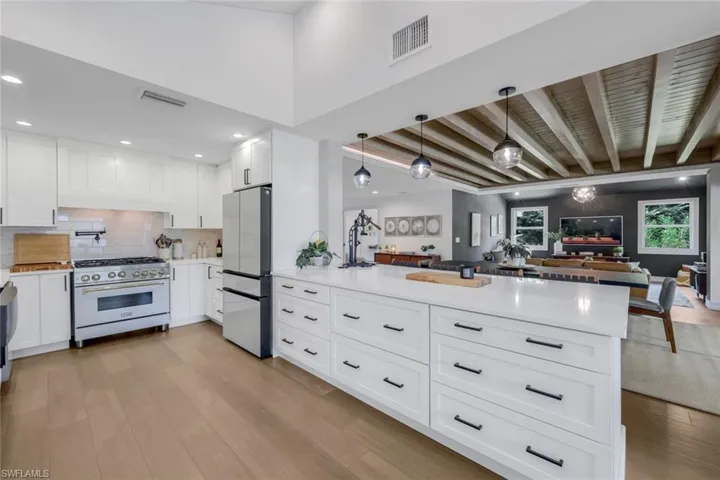 Kitchen featuring decorative light fixtures, stainless steel refrigerator, beamed ceiling, decorative backsplash, and designer stove