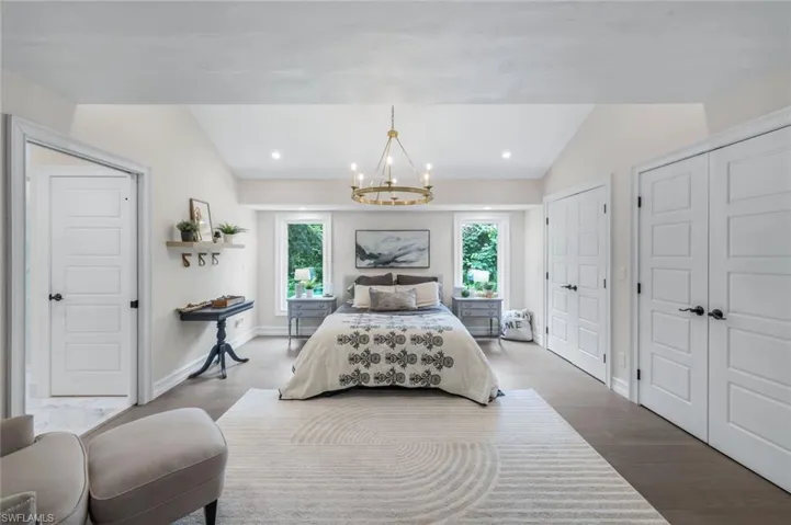 Bedroom featuring wood-type flooring, a notable chandelier, lofted ceiling, and two closets