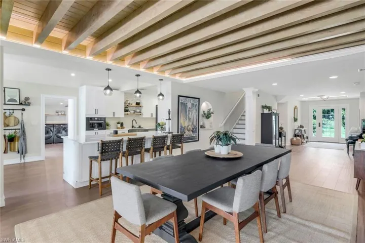 Dining space with light hardwood / wood-style flooring, beam ceiling, decorative columns, sink, and washing machine and dryer