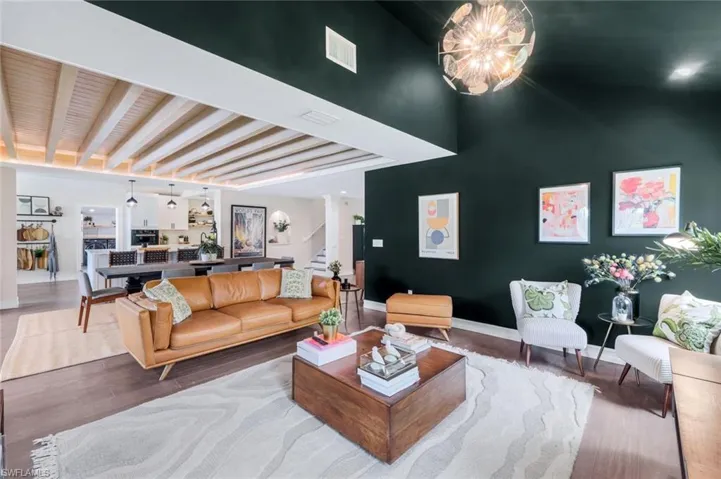 Living room featuring dark hardwood / wood-style flooring, beam ceiling, a notable chandelier, and ornate columns