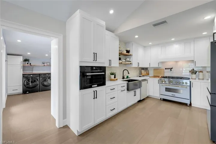 Kitchen featuring backsplash, light wood-type flooring, sink, black appliances, and separate washer and dryer