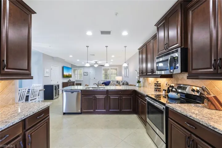 Kitchen featuring backsplash, light stone counters, ceiling fan, stainless steel appliances, and decorative light fixtures