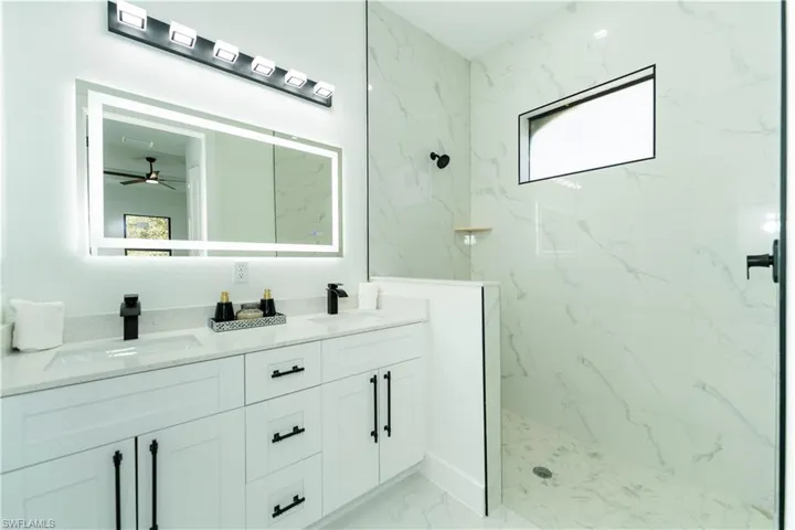 Bathroom featuring ceiling fan, vanity, plenty of natural light, and tiled shower