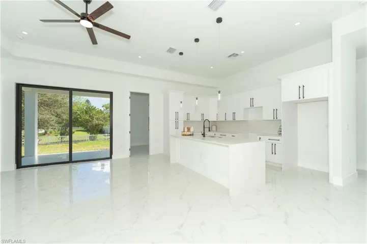 Kitchen featuring white cabinetry, a kitchen island with sink, ceiling fan, and pendant lighting