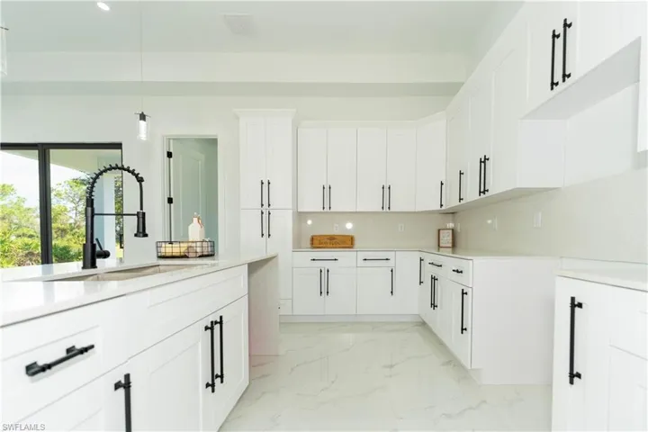 Kitchen with white cabinetry, hanging light fixtures, sink, and backsplash