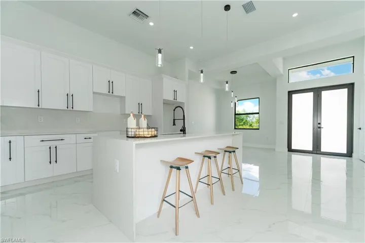 Kitchen with a kitchen breakfast bar, a kitchen island with sink, white cabinets, pendant lighting, and french doors