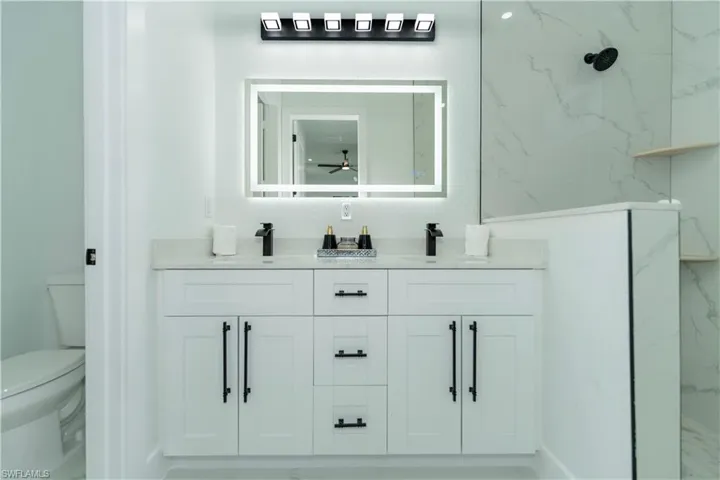 Bathroom featuring toilet, vanity, a tile shower, and ceiling fan