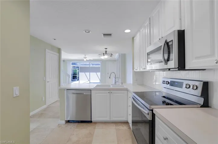 Kitchen with sink, white cabinets, kitchen peninsula, decorative backsplash, and appliances with stainless steel finishes