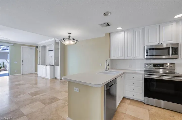Kitchen with sink, kitchen peninsula, decorative light fixtures, white cabinetry, and appliances with stainless steel finishes