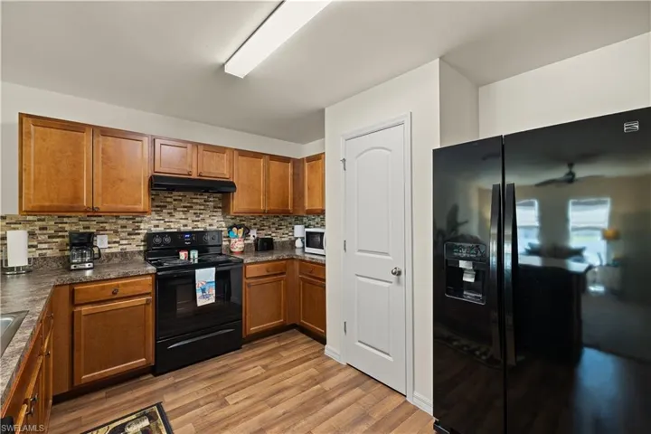 Kitchen featuring light hardwood / wood-style flooring, ceiling fan, black appliances, and tasteful backsplash