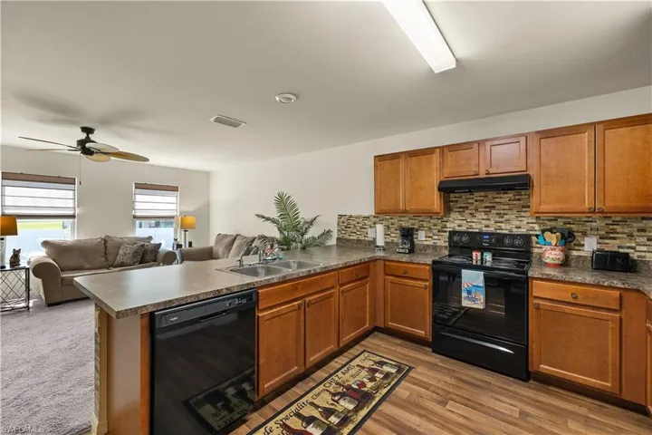 Kitchen with tasteful backsplash, black appliances, light hardwood / wood-style floors, sink, and kitchen peninsula