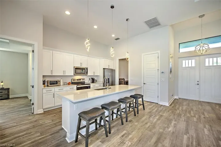 Kitchen with white cabinets, hanging light fixtures, a center island with sink, hardwood / wood-style flooring, and appliances with stainless steel finishes