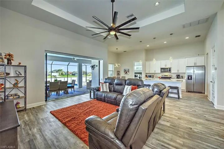 Living room with a raised ceiling, ceiling fan, and light wood-type flooring