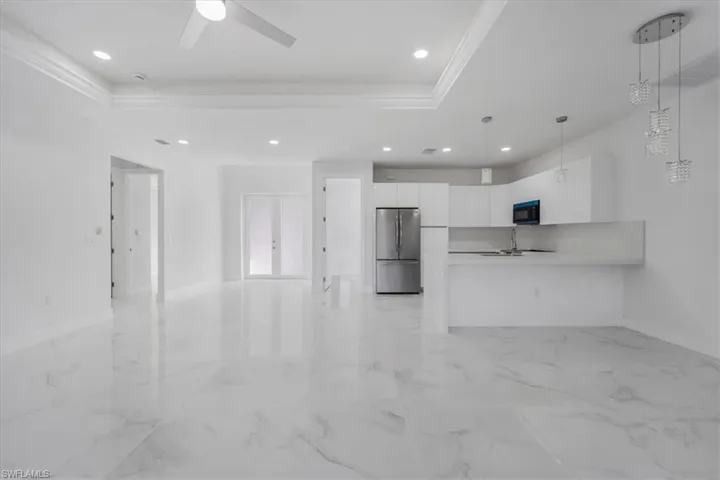 Unfurnished living room with a raised ceiling, crown molding, sink, and ceiling fan