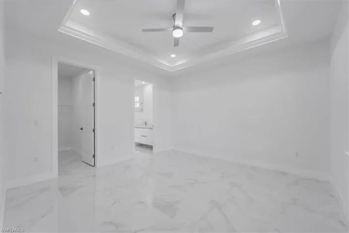 Unfurnished bedroom with connected bathroom, a tray ceiling, a spacious closet, and ceiling fan