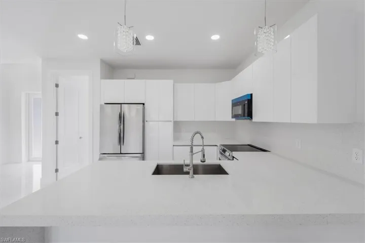 Kitchen featuring white cabinetry, stainless steel fridge, sink, and pendant lighting