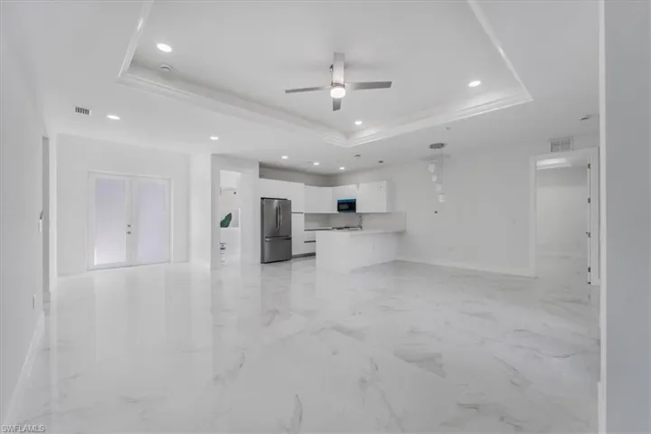 Unfurnished living room featuring ceiling fan, french doors, sink, and a tray ceiling