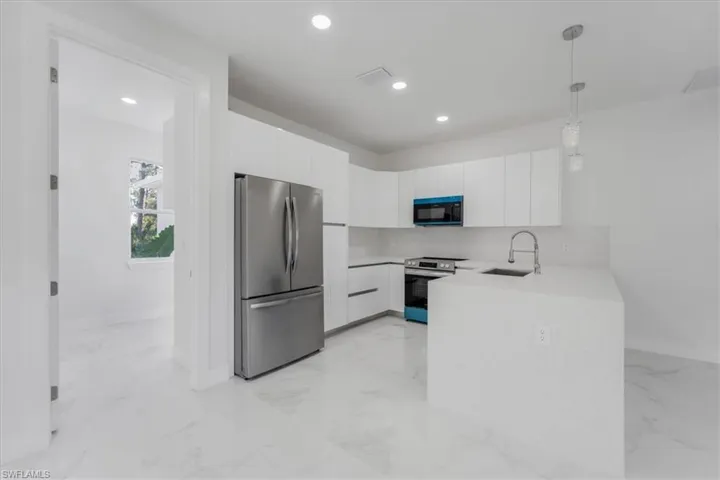 Kitchen featuring sink, white cabinetry, hanging light fixtures, and appliances with stainless steel finishes