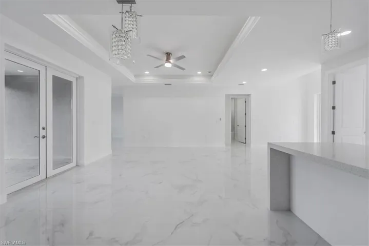 Empty room featuring ceiling fan with notable chandelier, a raised ceiling, ornamental molding, and french doors