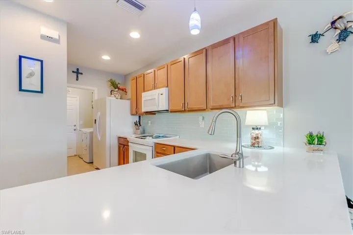 Kitchen with decorative light blue subway backsplash, blanco undermount sink, pendant lighting, and white appliances