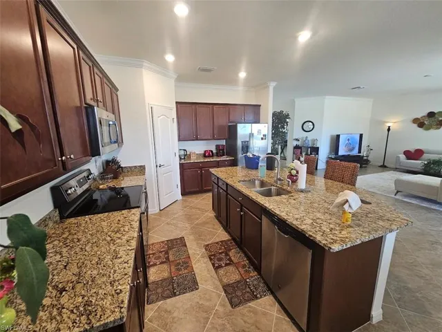 Kitchen with stainless steel appliances, sink, light stone countertops, and a kitchen island with sink