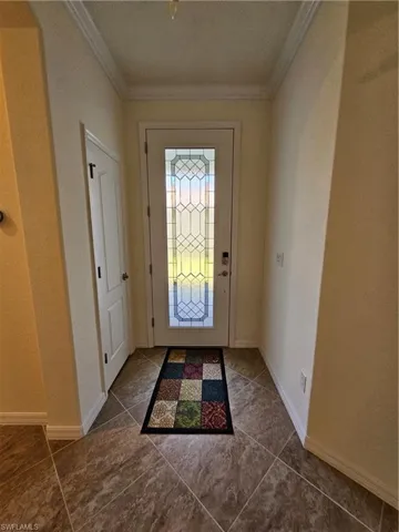 Doorway with dark tile flooring and crown molding