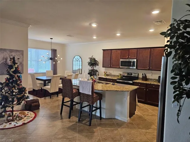 Kitchen featuring dark brown cabinetry, decorative light fixtures, a center island with sink, a kitchen breakfast bar, and stainless steel appliances