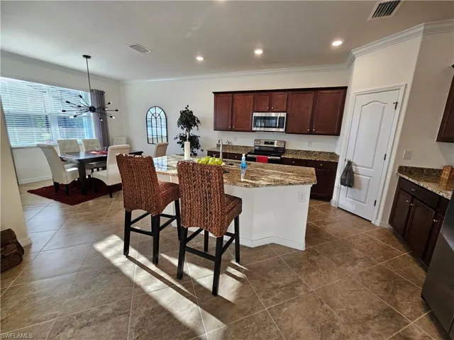 Kitchen with ceiling fan, light stone countertops, an island with sink, appliances with stainless steel finishes, and pendant lighting