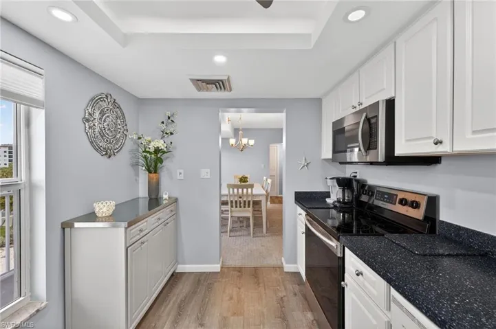 Kitchen featuring stainless steel appliances, white cabinetry, recessed lighting, light wood-style flooring, and a tray ceiling. - Virtually Edited Image