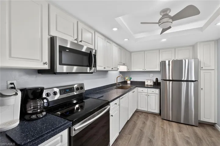 Kitchen featuring stainless steel appliances, classic white cabinetry, ceiling fan, recessed lighting, and light wood-style flooring. - Virtually Edited Image