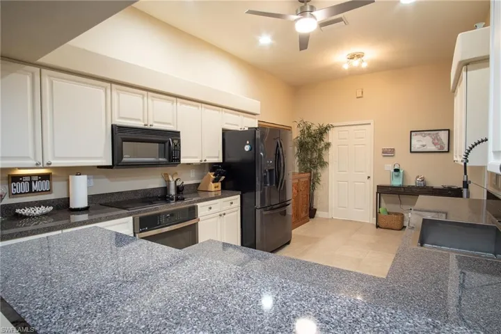 Kitchen with ceiling fan, light tile patterned floors, kitchen peninsula, white cabinets, and black appliances