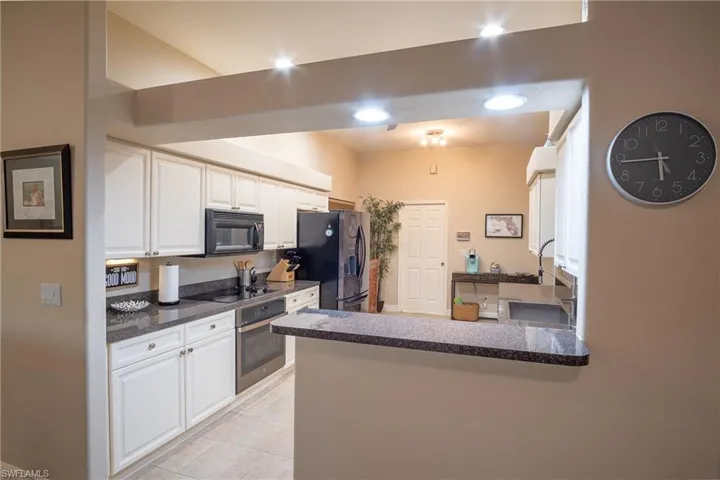Kitchen featuring kitchen peninsula, white cabinets, light tile patterned flooring, and black appliances