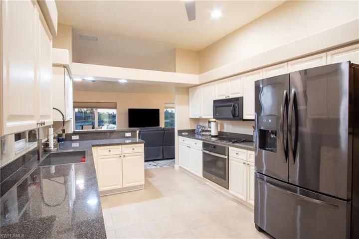 Kitchen featuring light tile patterned flooring, sink, dark stone counters, and black appliances