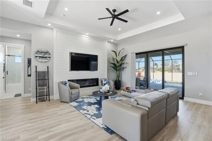 Living room featuring a raised ceiling, ceiling fan, light wood-type flooring, a large fireplace, and recessed lighting