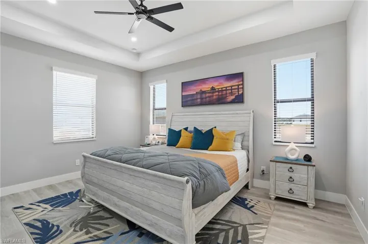 Bedroom with a raised ceiling, light wood-type flooring, and a ceiling fan