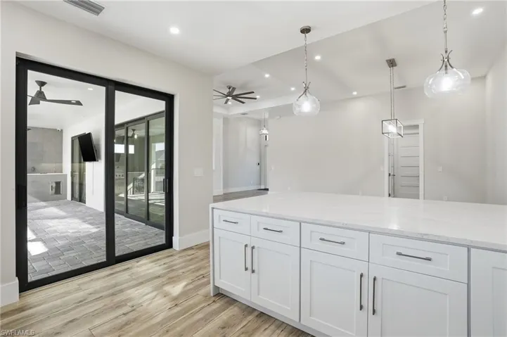 Kitchen with pendant lighting, white cabinetry, light wood-style floors, light stone counters, and a ceiling fan