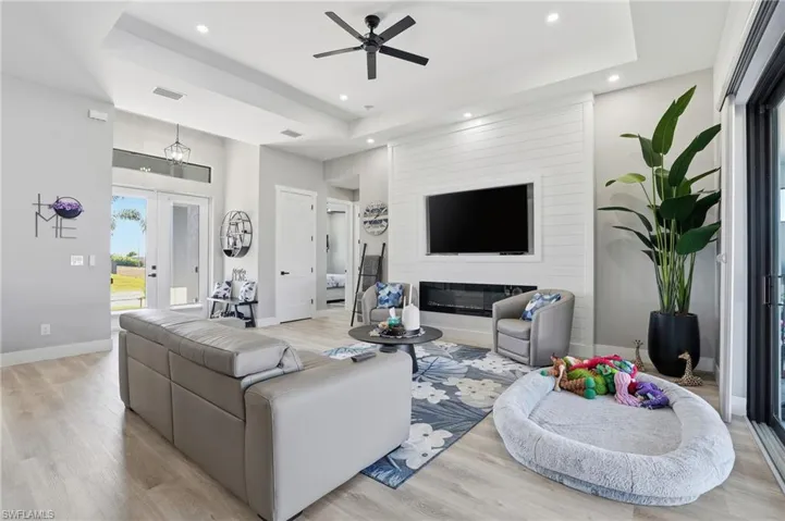 Living area featuring a ceiling fan, light wood finished floors, a raised ceiling, a glass covered fireplace, and recessed lighting
