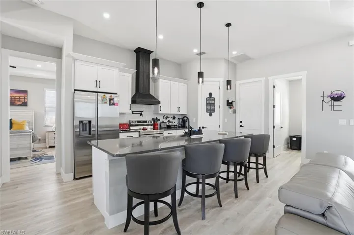 Kitchen featuring white cabinetry, stainless steel appliances, a kitchen bar, light wood-style flooring, and an island with sink
