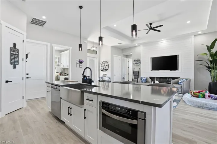 Kitchen featuring white cabinets, a kitchen island with sink, open floor plan, pendant lighting, and light wood-type flooring