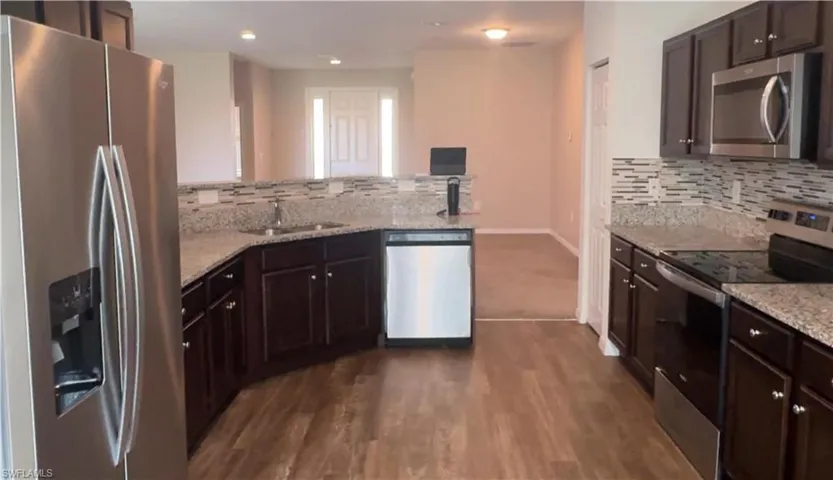 Kitchen with stainless steel appliances, light stone countertops, dark brown cabinets, a peninsula, and recessed lighting