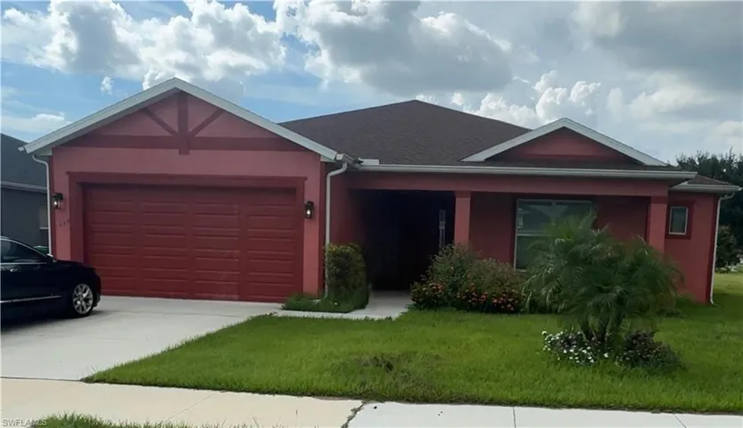 Ranch-style house with a front yard, stucco siding, a garage, and driveway