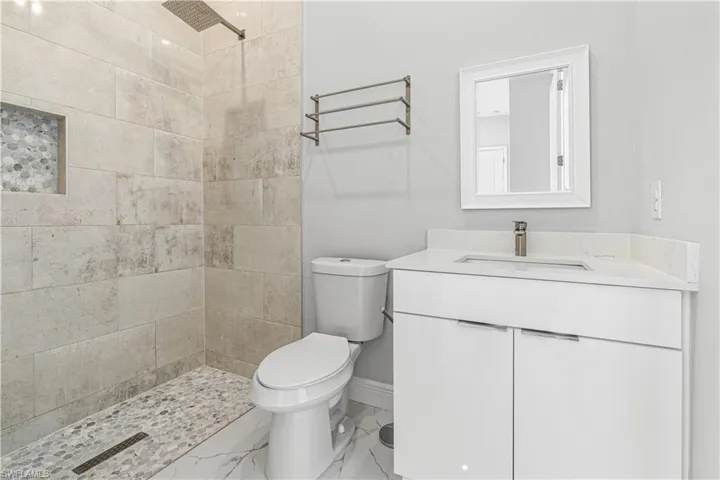 Bathroom with a tile shower, tile flooring, toilet, and large vanity