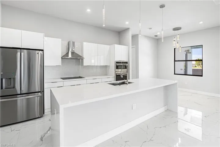 Kitchen with a center island, decorative light fixtures, stainless steel appliances, white cabinetry, and more