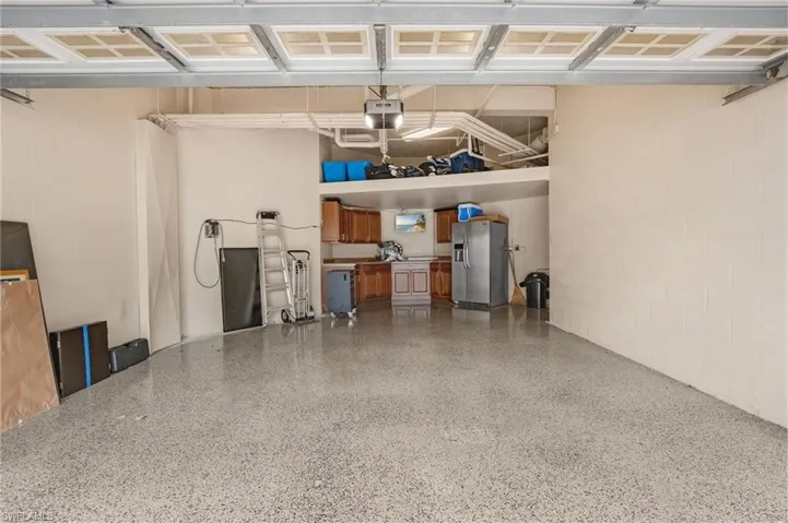 Spacious two-car garage with epoxy-finished floors, built-in cabinets, overhead storage, and included refrigerator.