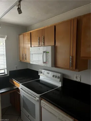 Kitchen with range, dark countertops, white microwave, and dishwasher