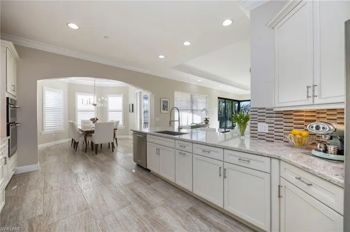Kitchen with crown molding, a peninsula, arched walkways, decorative backsplash, and white cabinets