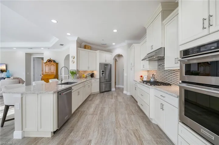 Kitchen with stainless steel appliances, decorative backsplash, a kitchen bar, arched walkways, and a peninsula