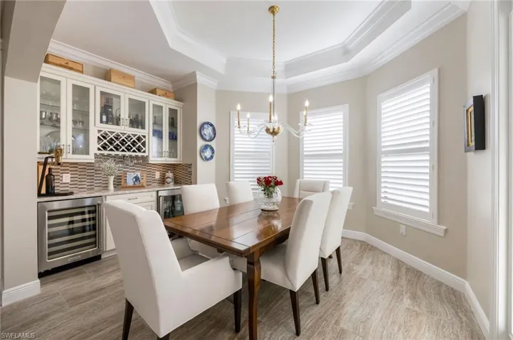 Dining space featuring wine cooler, hanging lights, a bar, a tray ceiling, and wood finish floors