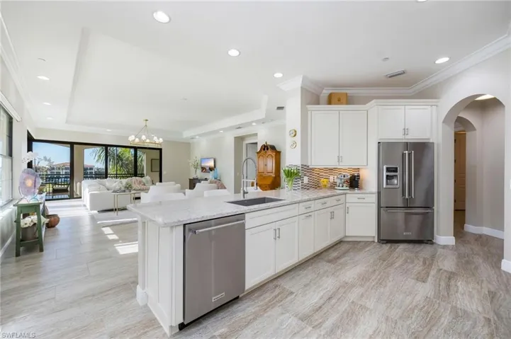 Kitchen featuring white cabinets, arched walkways, stainless steel appliances, a raised ceiling, and tasteful backsplash
